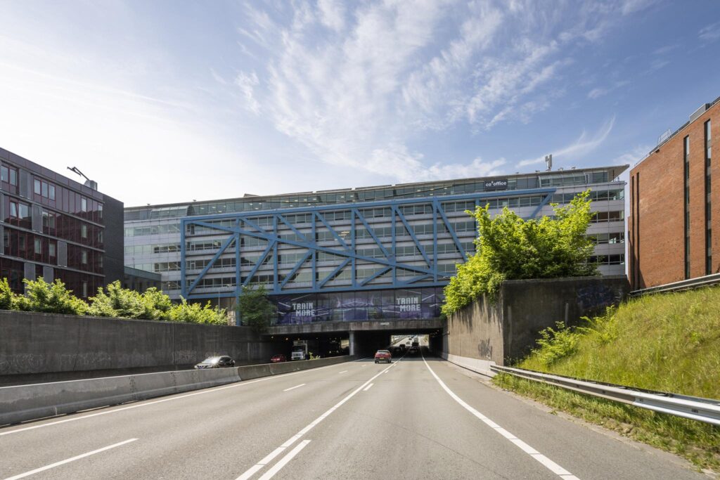 View of the Bos en Lommerplein building with blue structural beams spanning over a highway tunnel in Amsterdam.